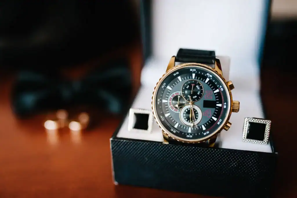 Automatic Watch Winders Explained: From Basic Settings to Pro Tips 1 A gold-trimmed wristwatch with a black dial and red accents presented in a box with cufflinks in the background, emphasizing the importance of using an automatic watch winder to maintain its precision and readiness.